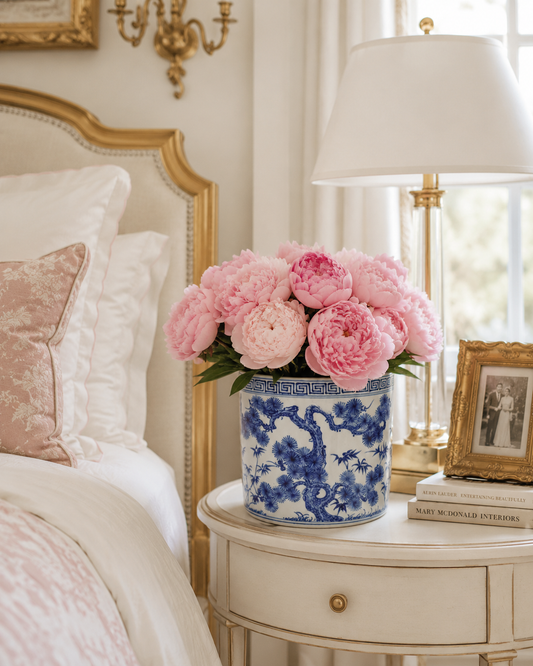 a vase of pink flowers on a table next to a bed