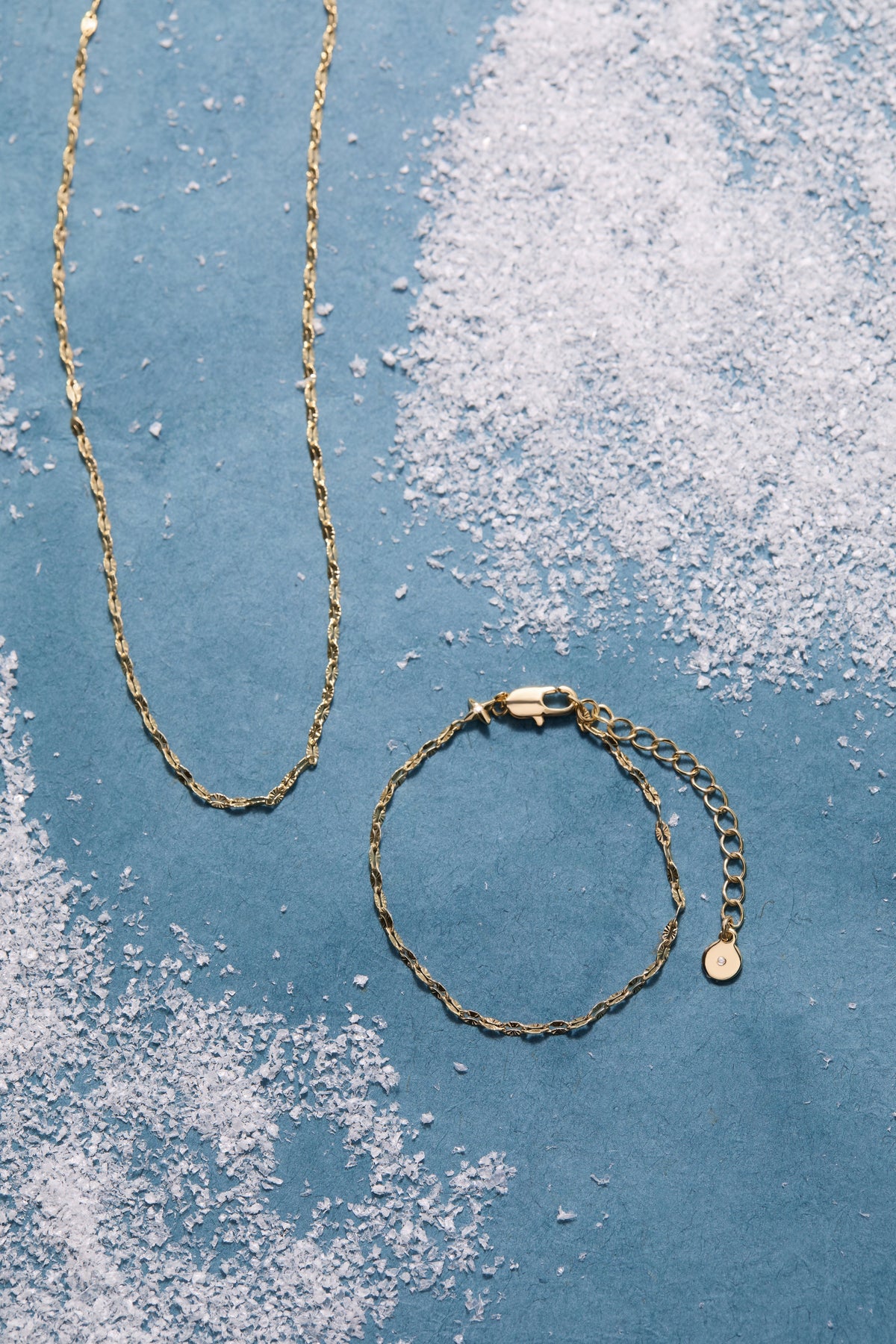 a gold chain and bracelet on a blue surface