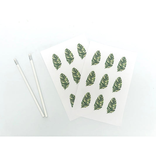 two white cards with green leaves on them next to two pencils