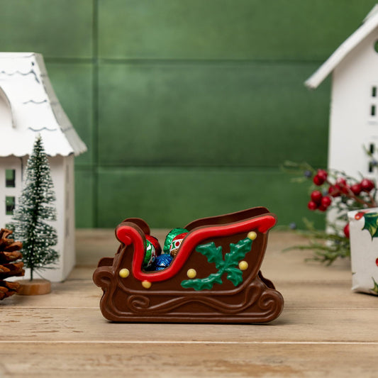 a chocolate sleigh with candy in it next to a couple houses