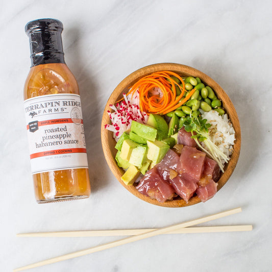 a bowl of raw fish and vegetables next to a bottle of sauce