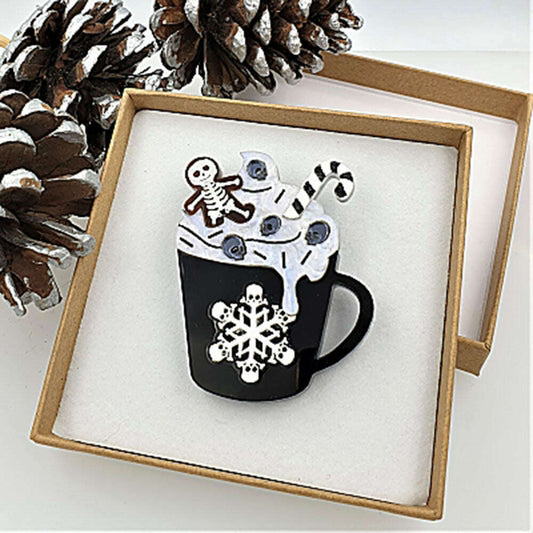 a pin in a box with a mug of hot chocolate and a couple pine cones