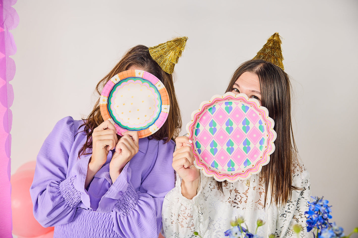 two women wearing party hats and holding plates