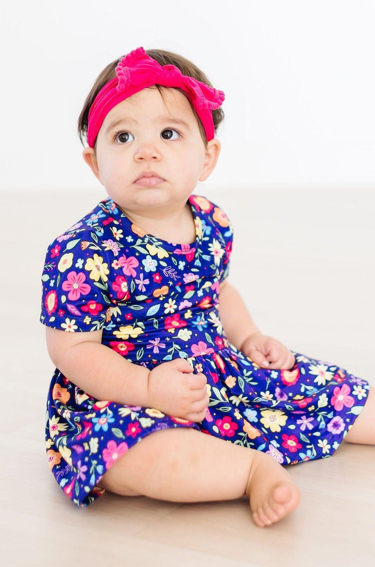 a baby girl wearing a flowered dress and a pink headband