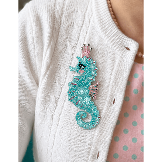 a woman wearing a white sweater with a blue seahorse brooch
