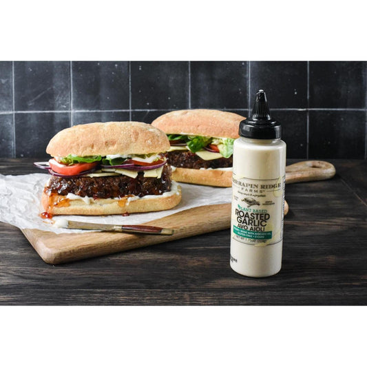two burgers on a cutting board next to a bottle of sauce