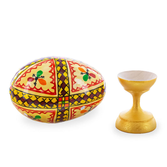 a yellow egg with red and blue designs next to a gold egg