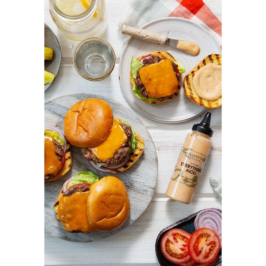 a group of burgers on plates next to a bottle of sauce
