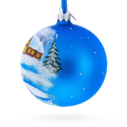 a blue christmas ornament with a house and trees painted on it