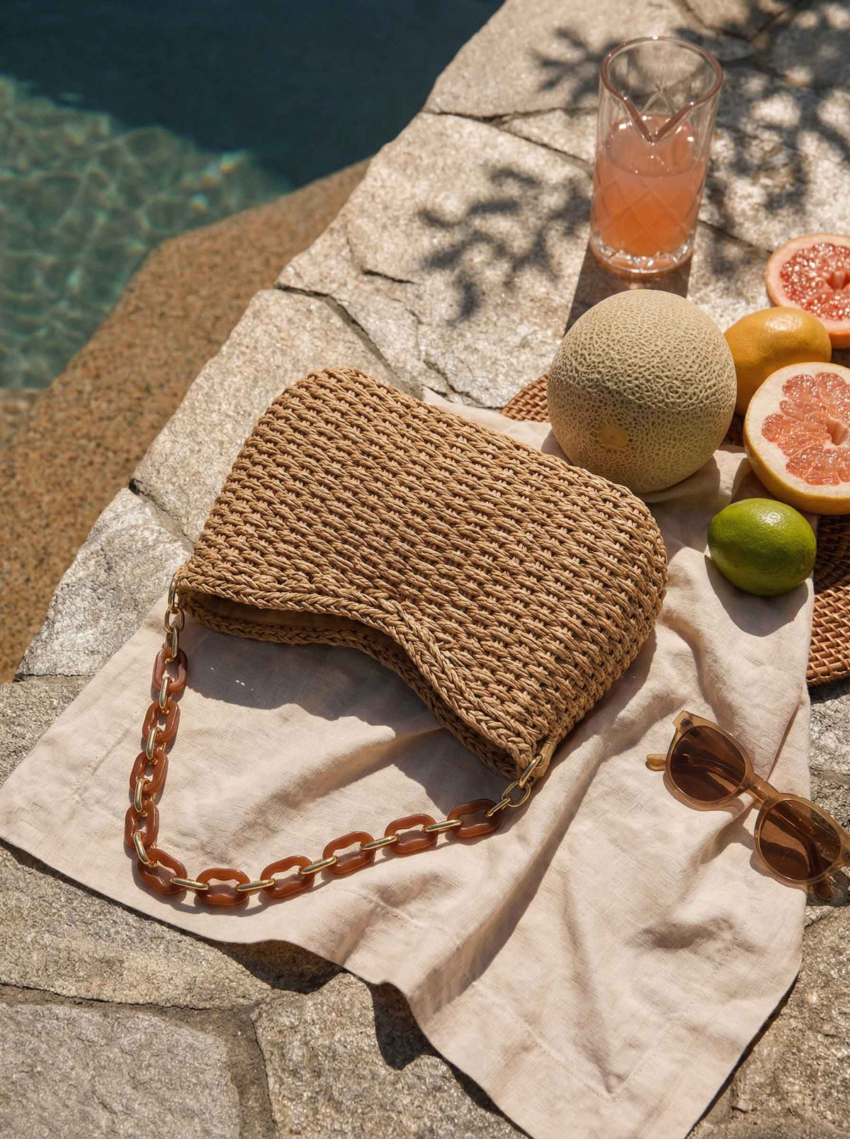 a straw bag and fruit on a towel next to a pool