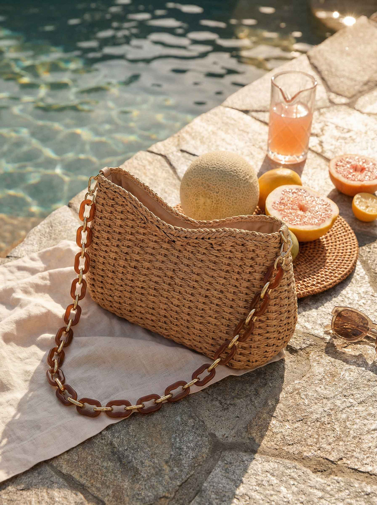 a straw bag and fruit on a towel next to a drink