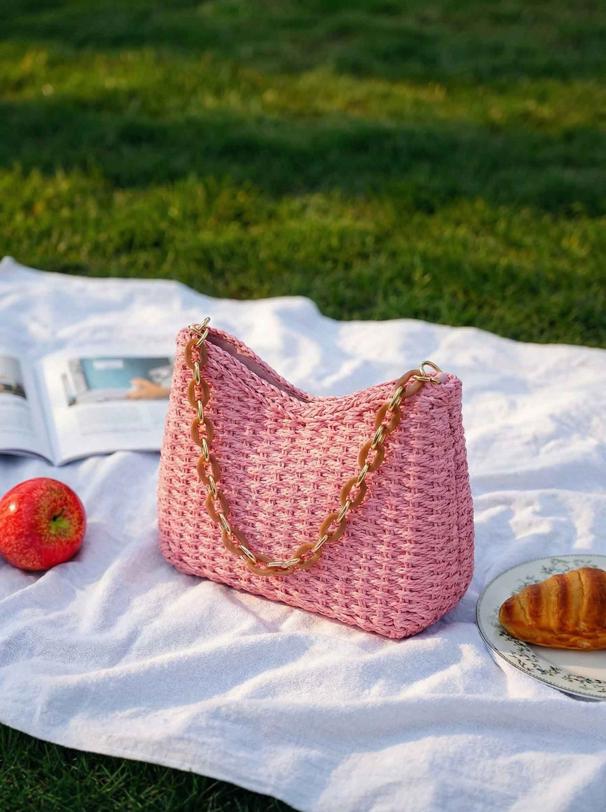 a pink bag and a plate of croissant on a blanket