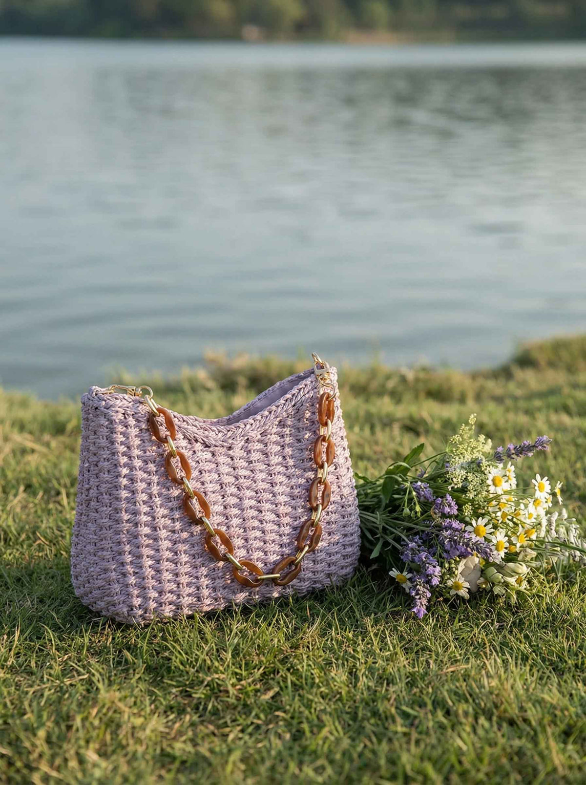 a purse and flowers on grass by water