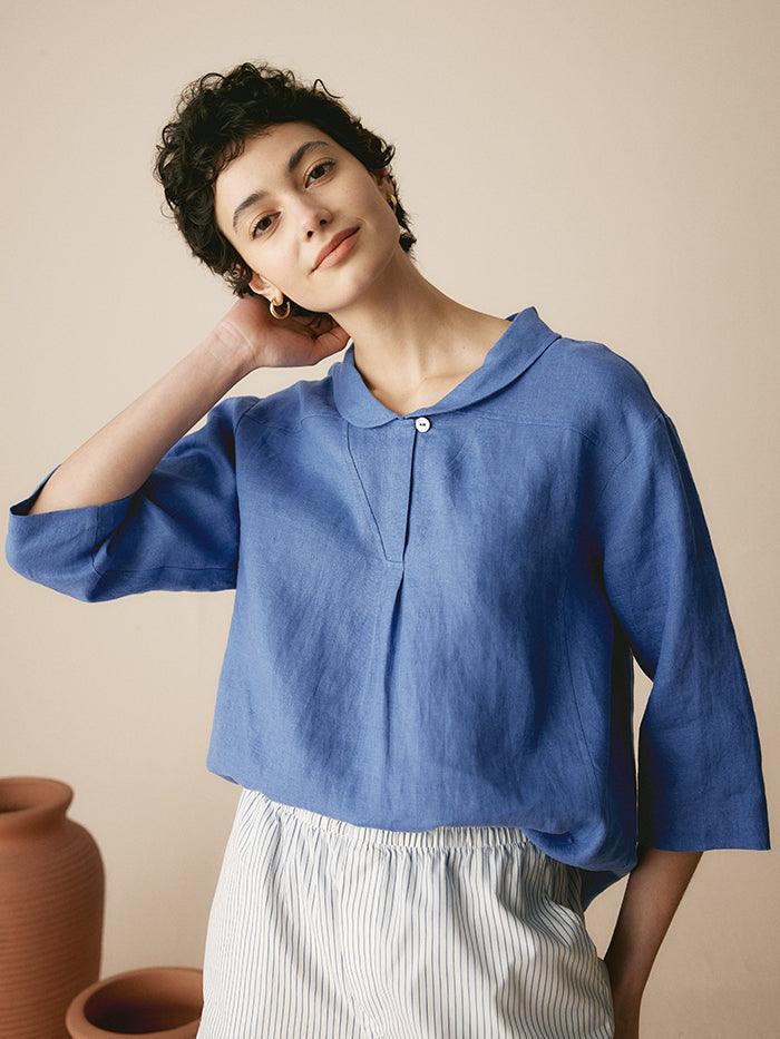 a woman with short hair wearing a blue shirt and white pants