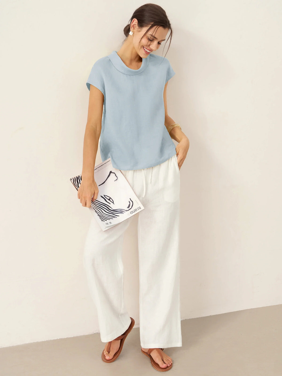 a woman in white pants and blue shirt holding a book