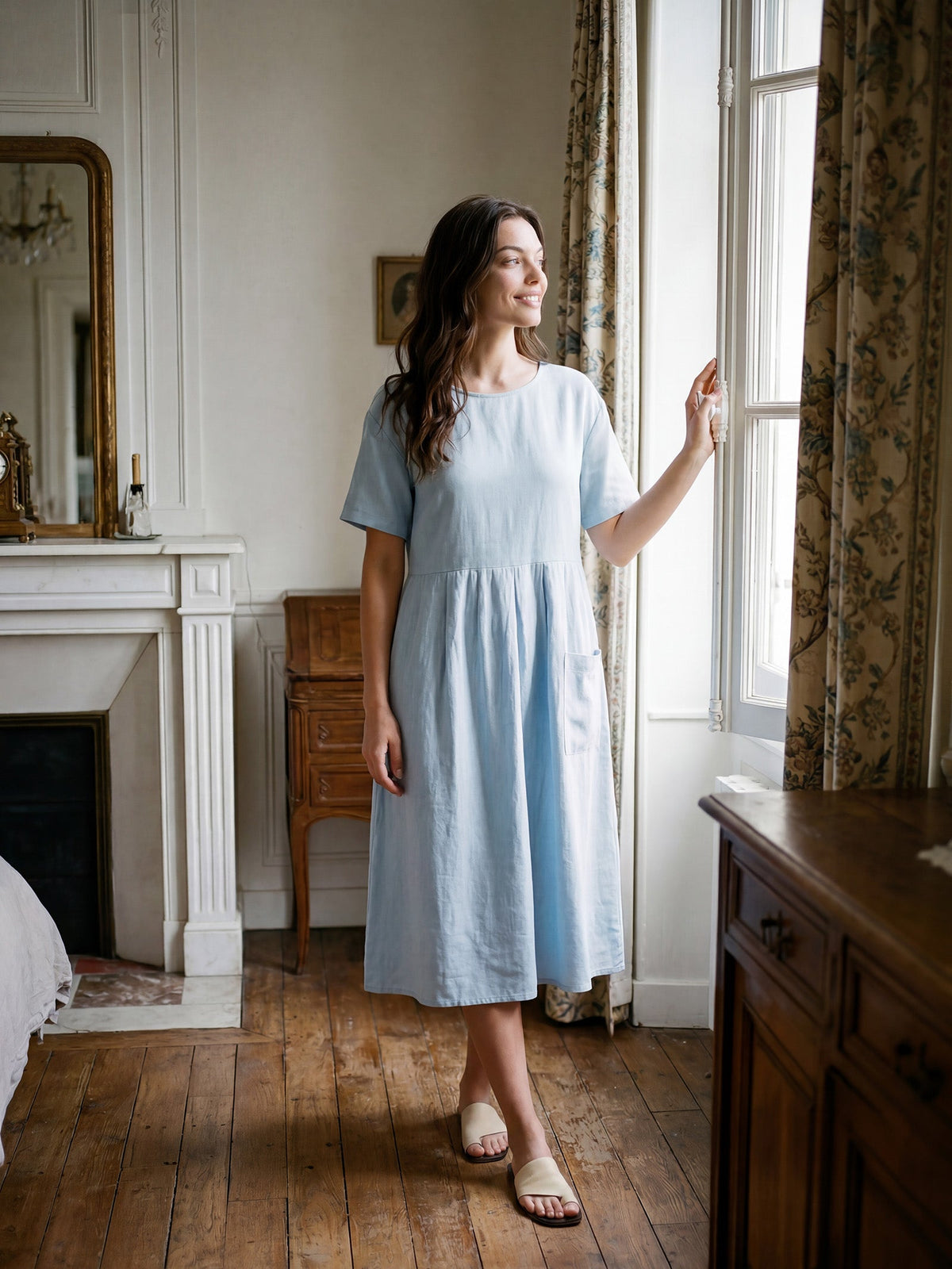 a woman in a blue dress standing in front of a window