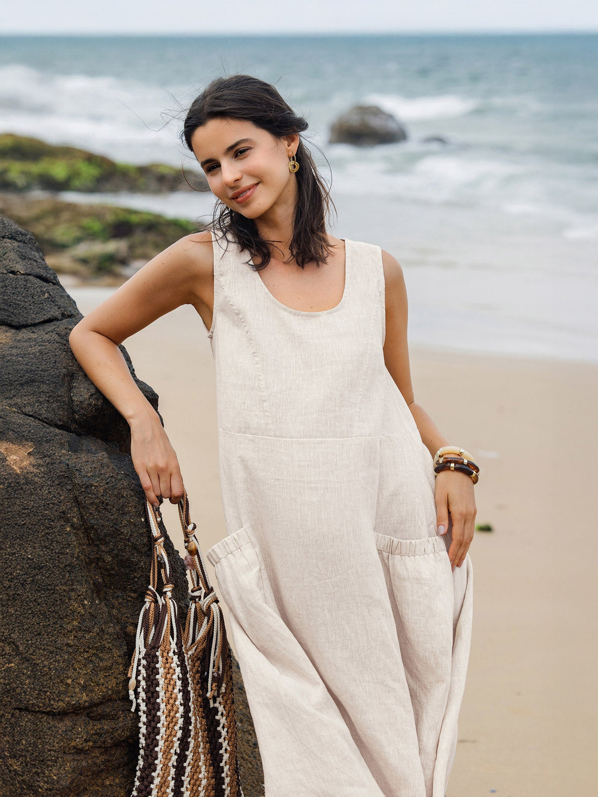 a woman in a white dress leaning against a rock on a beach