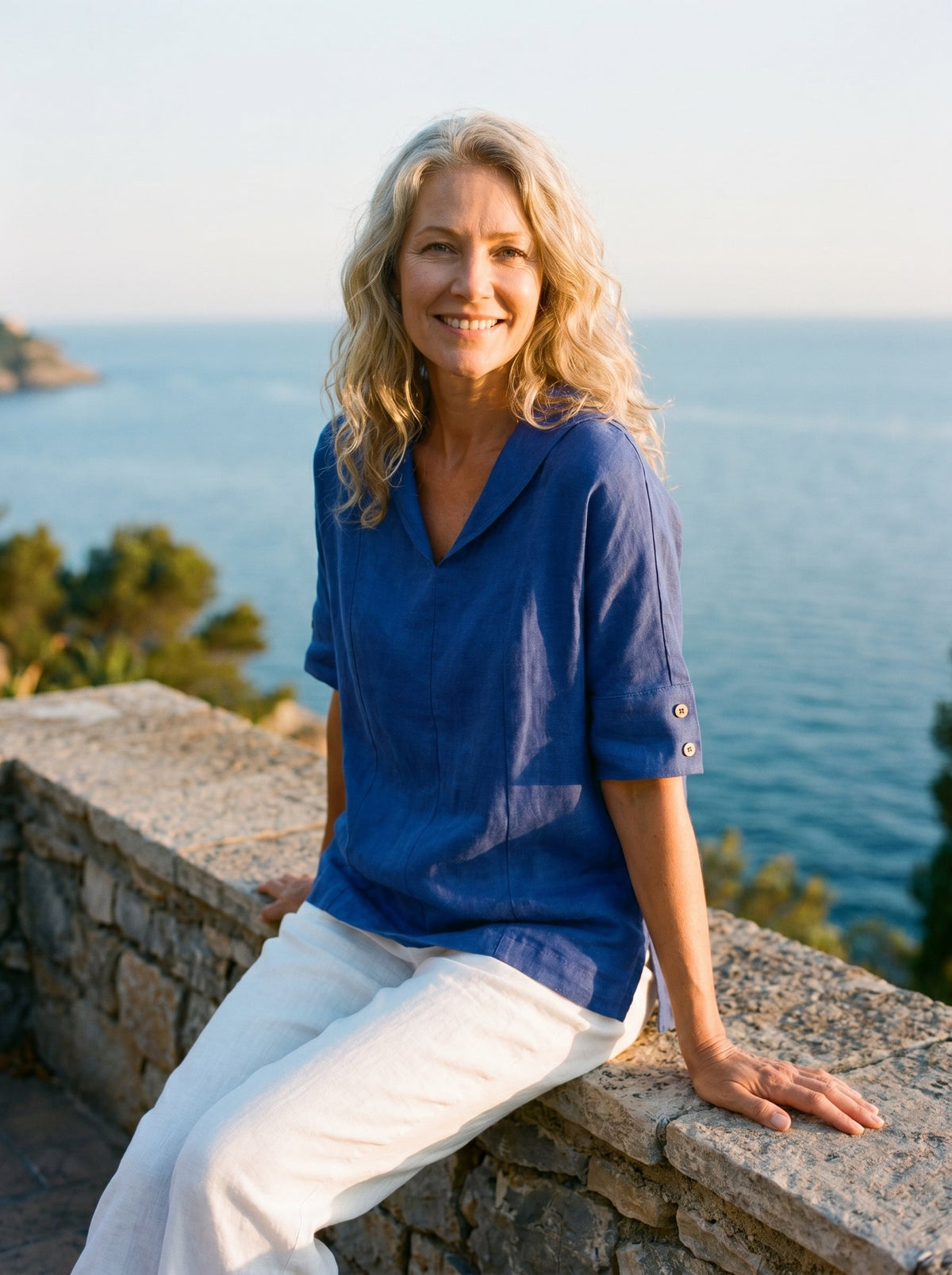 a woman sitting on a ledge with a body of water in the background