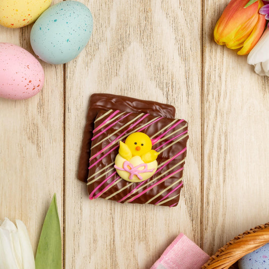 a chocolate square with a yellow chick on it next to colorful eggs and tulips