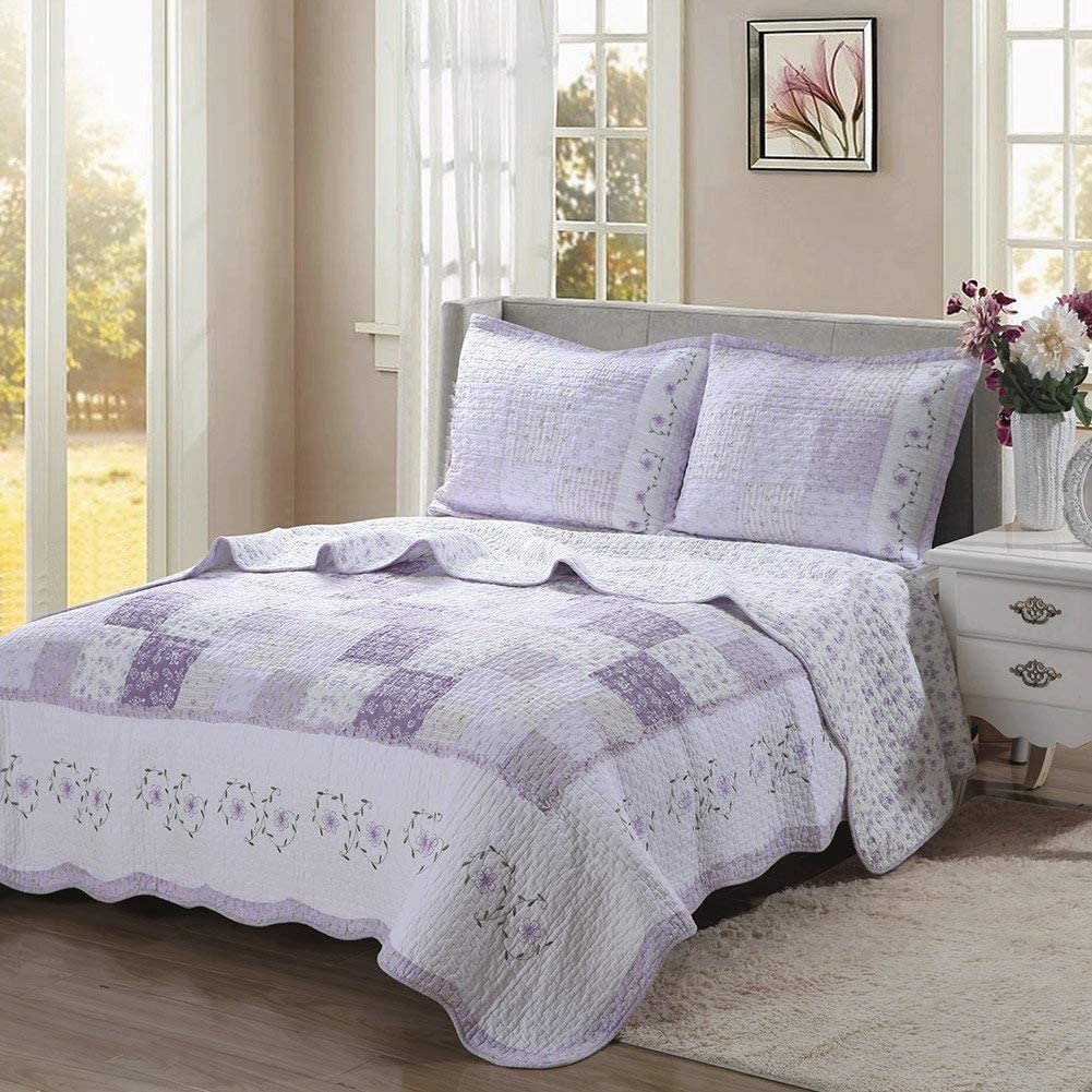 a bed with a quilt and a vase of flowers in front of windows