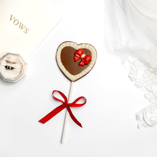 a heart shaped lollipop with a red bow and a white envelope