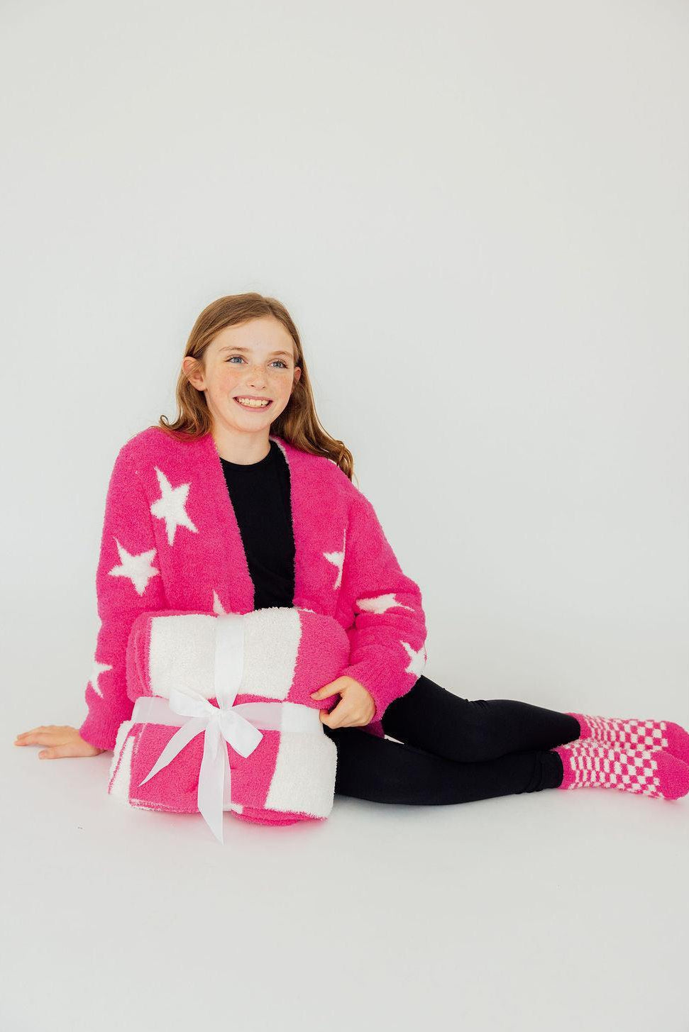 a girl sitting on the floor with a pink robe and white towels