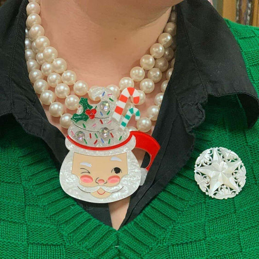 a person wearing a green sweater with a necklace and brooch