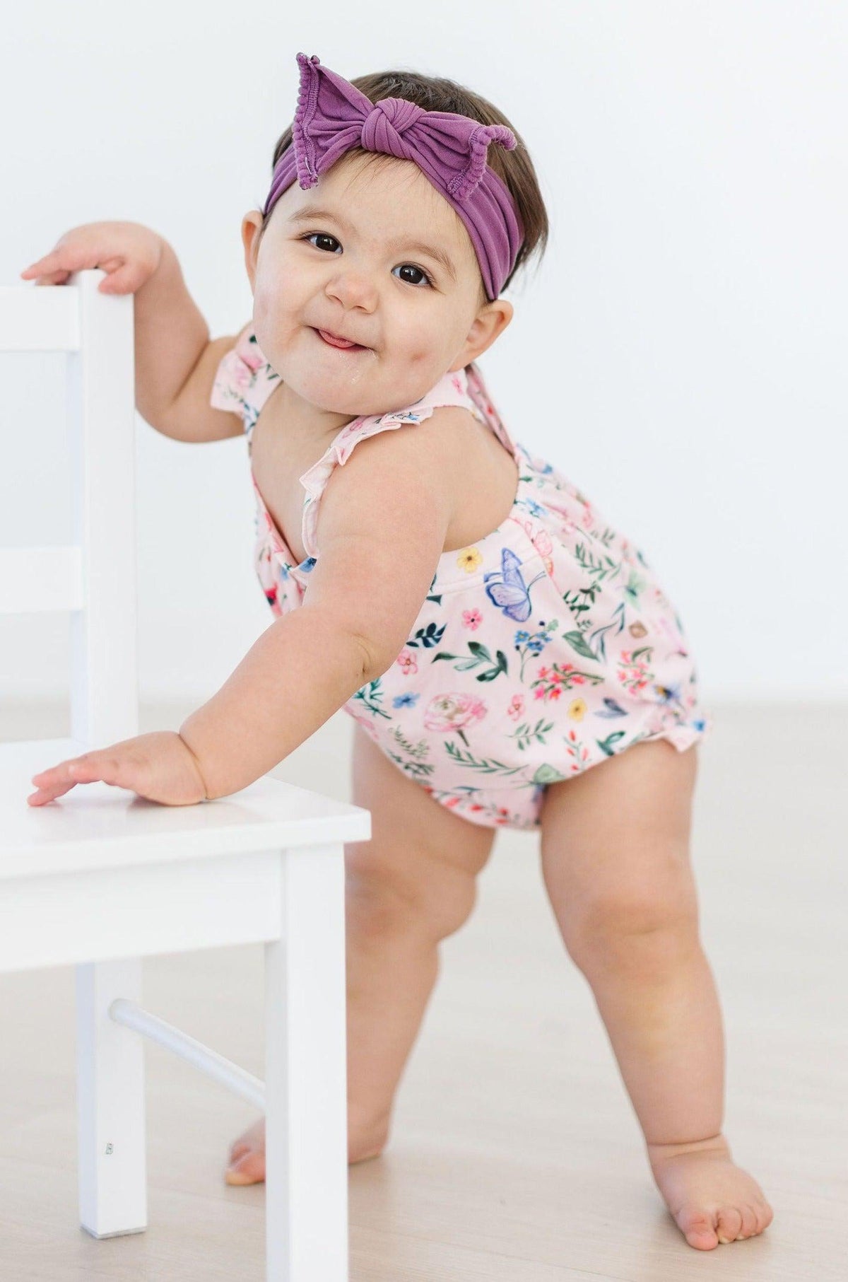 a baby girl wearing a headband and standing on a chair