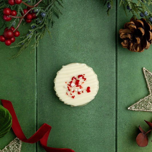 a white cookie with red sprinkles and pine cones on a green surface
