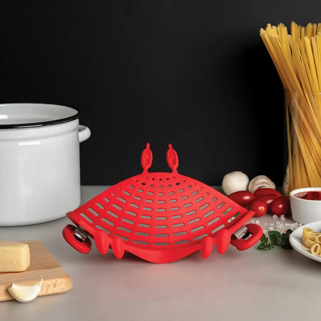a red strainer on a counter next to a white pot and food