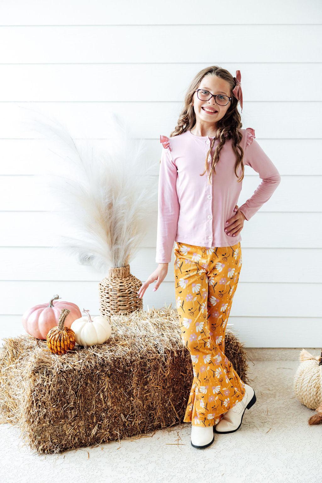 a girl standing in front of a stack of hay