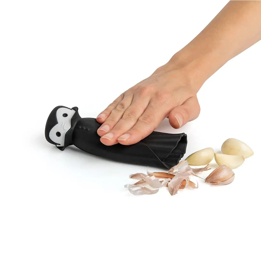 a hand holding a black object next to garlic cloves