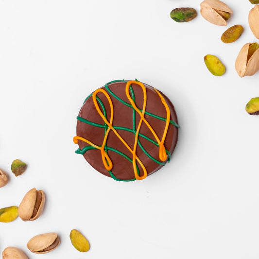 a chocolate cookie with orange and green icing and pistachios