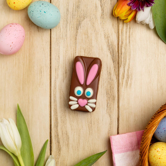 a chocolate bunny with a bunny face next to eggs and flowers