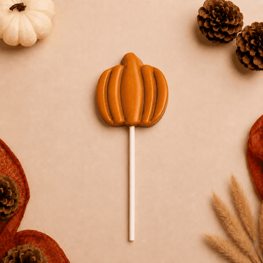a lollipop in the shape of a pumpkin surrounded by pine cones
