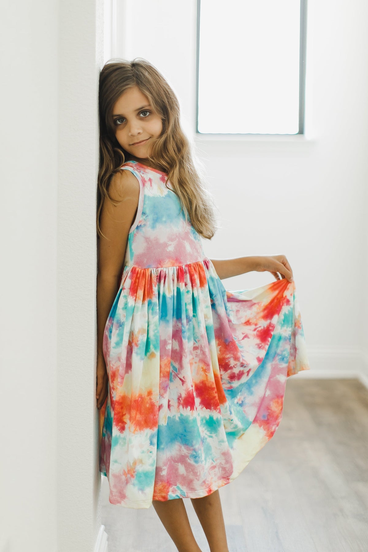a girl in a tie dye dress leaning against a wall