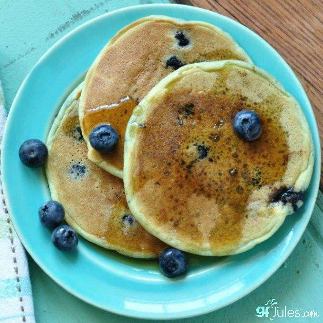 Stack of blueberry pancakes on a turquoise plate with blueberries scattered around.