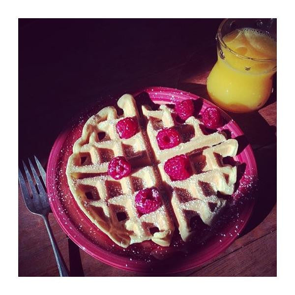 Waffles with raspberries on a pink plate with a glass of orange juice.