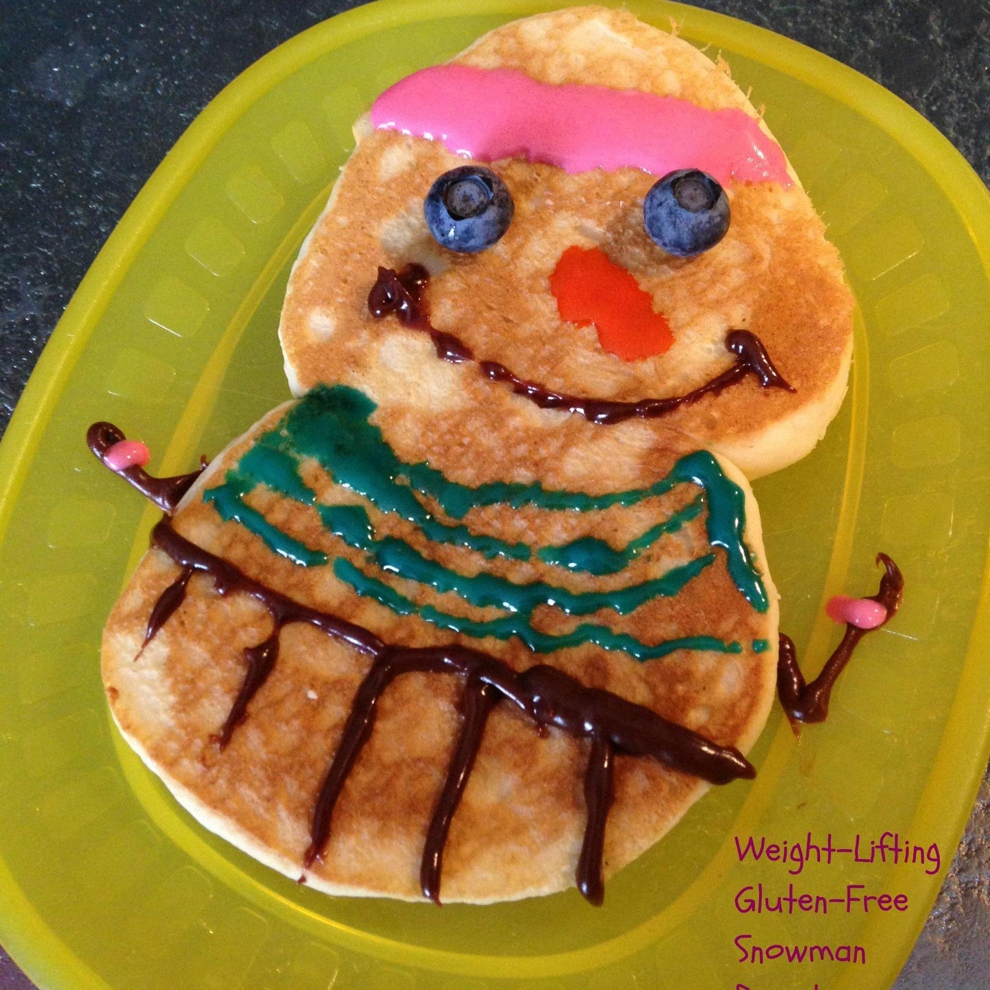 Pancake art shaped like a snowman on a yellow plate with 'Weight-Lifting Gluten-Free Snowman Pancake' text.