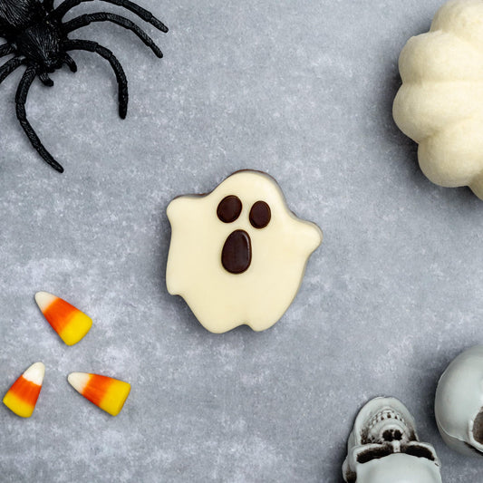 a white ghost cookie with a black spider and candy corn