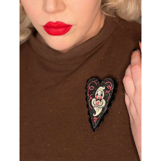 a woman wearing a brown shirt with a black heart brooch