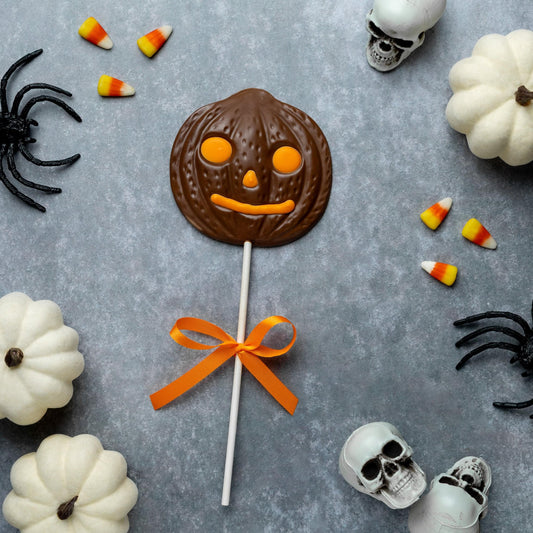 a chocolate candy on a stick surrounded by white pumpkins
