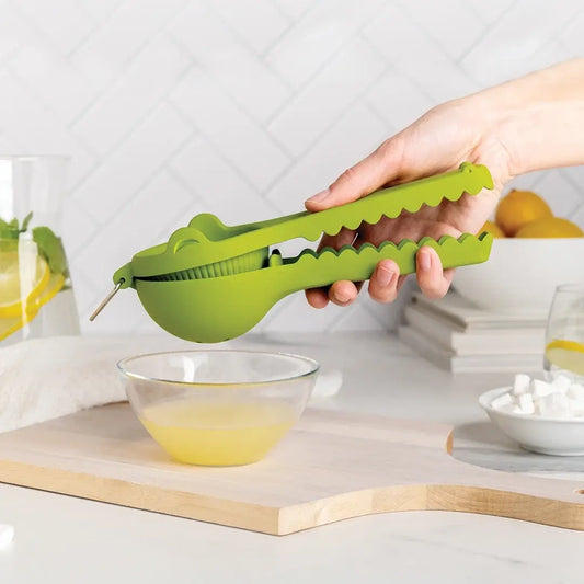 a hand holding a green lemon squeezer over a bowl of liquid