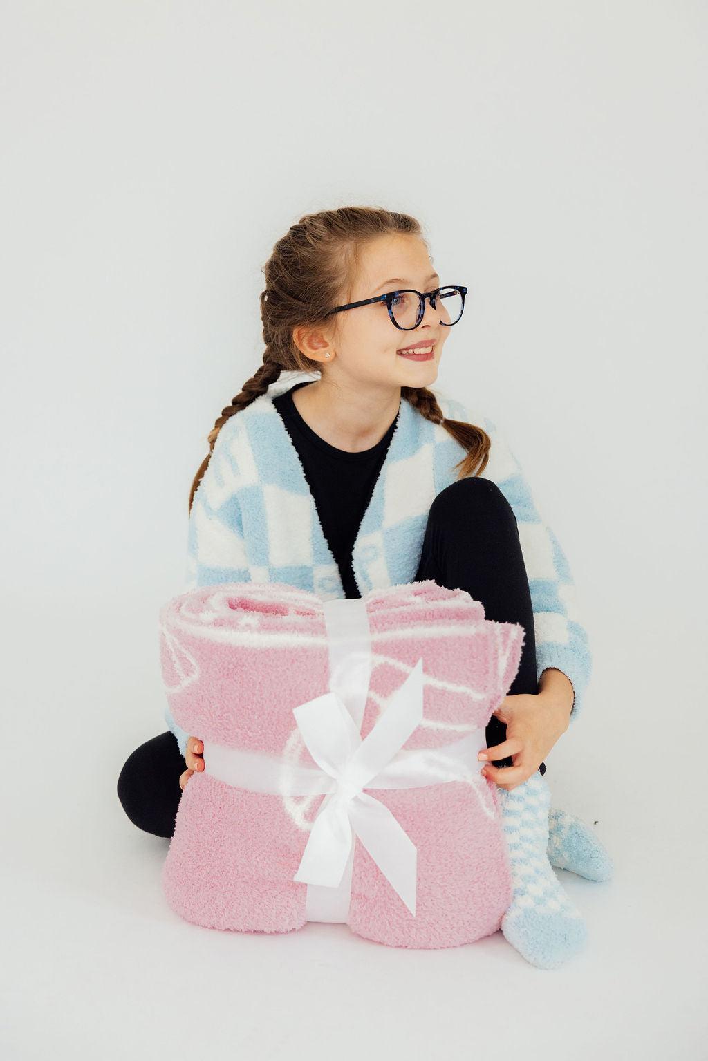 a girl sitting on the floor holding a pink blanket