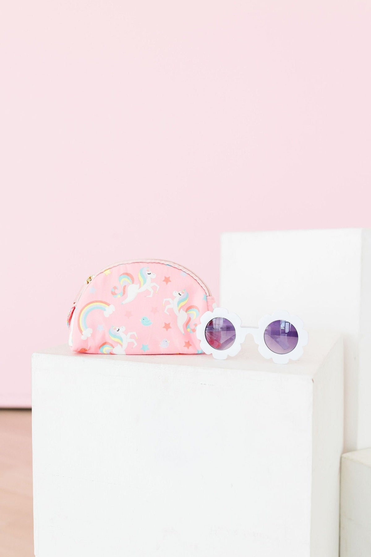a pink sunglasses and a pink pouch on a white cube