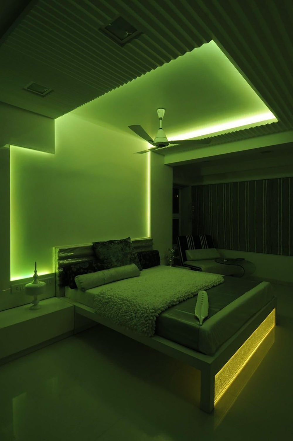a green lit bedroom with a bed and a ceiling fan