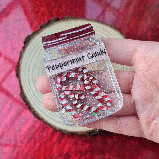 a hand holding a small plastic jar with glitter and candy canes