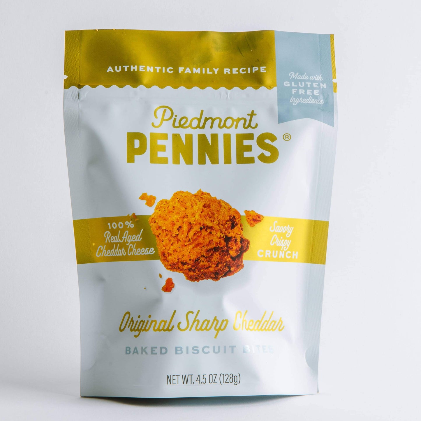 A stand-up pouch of Piedmont Pennies Original Sharp Biscuit with Cheese on a clean white background. The packaging features a white body with a gold top band and a central image of a cheesy biscuit and cheese slice.