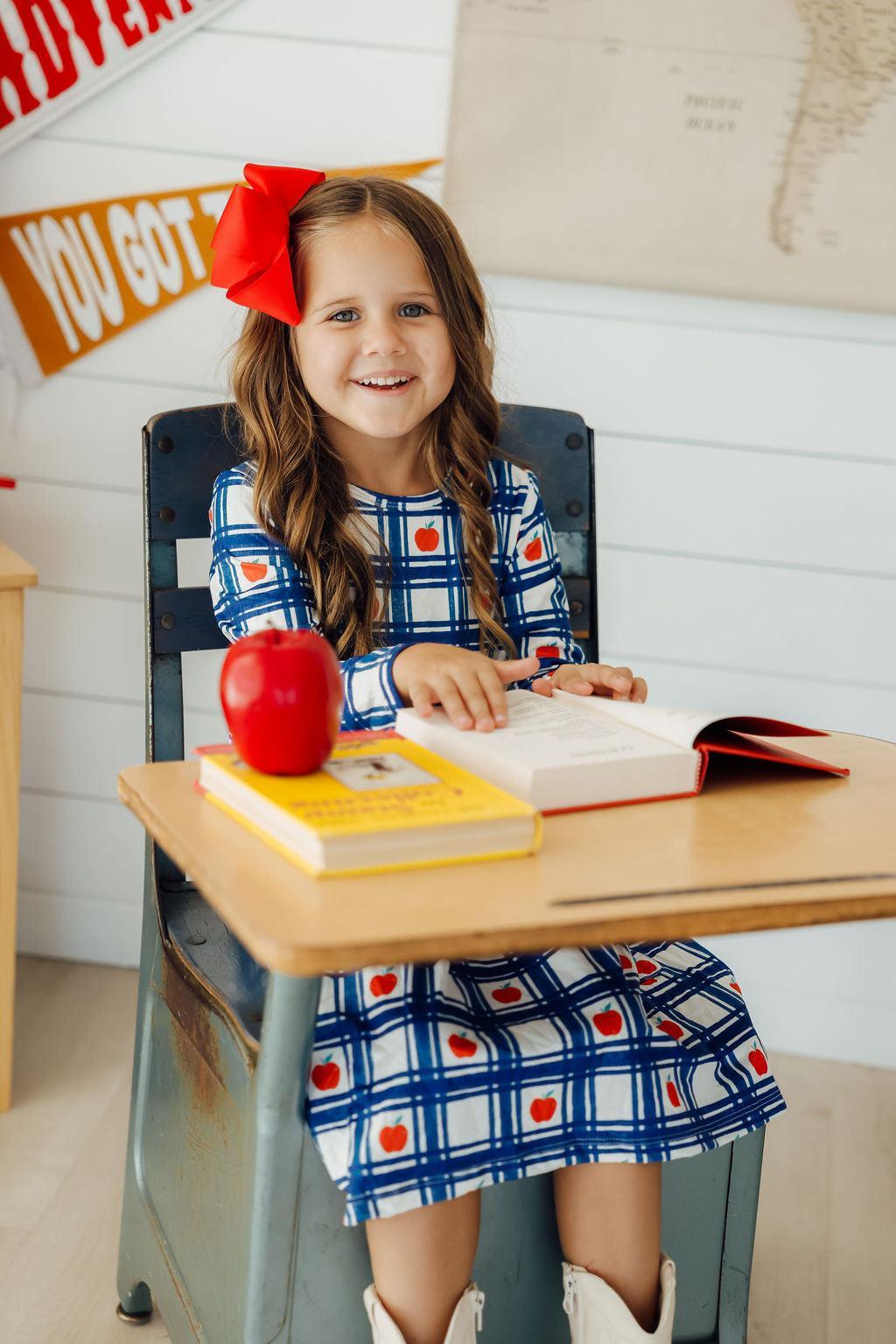 a girl sitting at a desk with a book and an apple