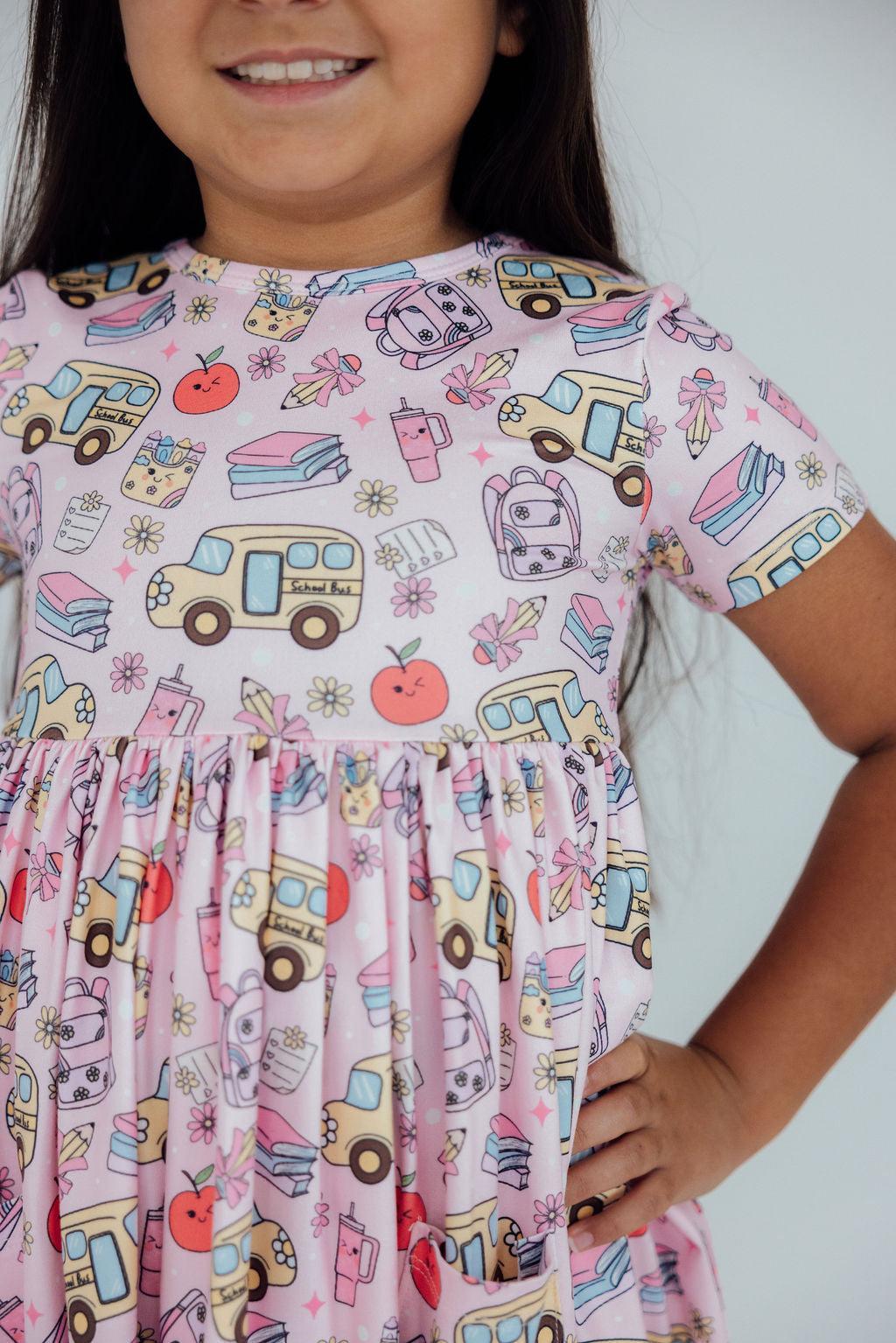 a girl wearing a dress with a picture of school bus and apple